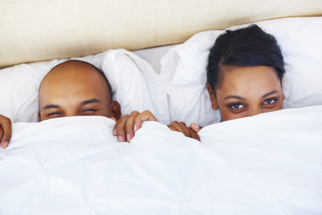 Young couple in bed doing peek-a-boo with you