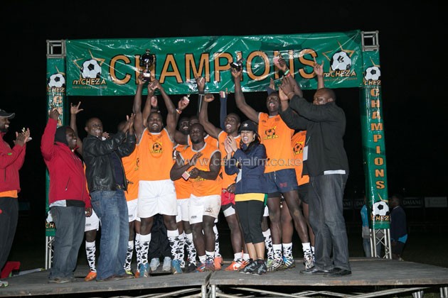 9585: mCHEZA 7s Winners Chipu Jackpot celebrate their victory alongside mCHEZA Chairman Philip Muema, mCHEZA Director Julie Gichuru and tournament Organizer Nills Achayo. The team, which was coached by Felix Ayange walked away with Ksh 500,000 after beating mCHEZA 295525 19-12. The tournament sought the expertise of the Kenya 7s players to nurture younger upcoming talented players.